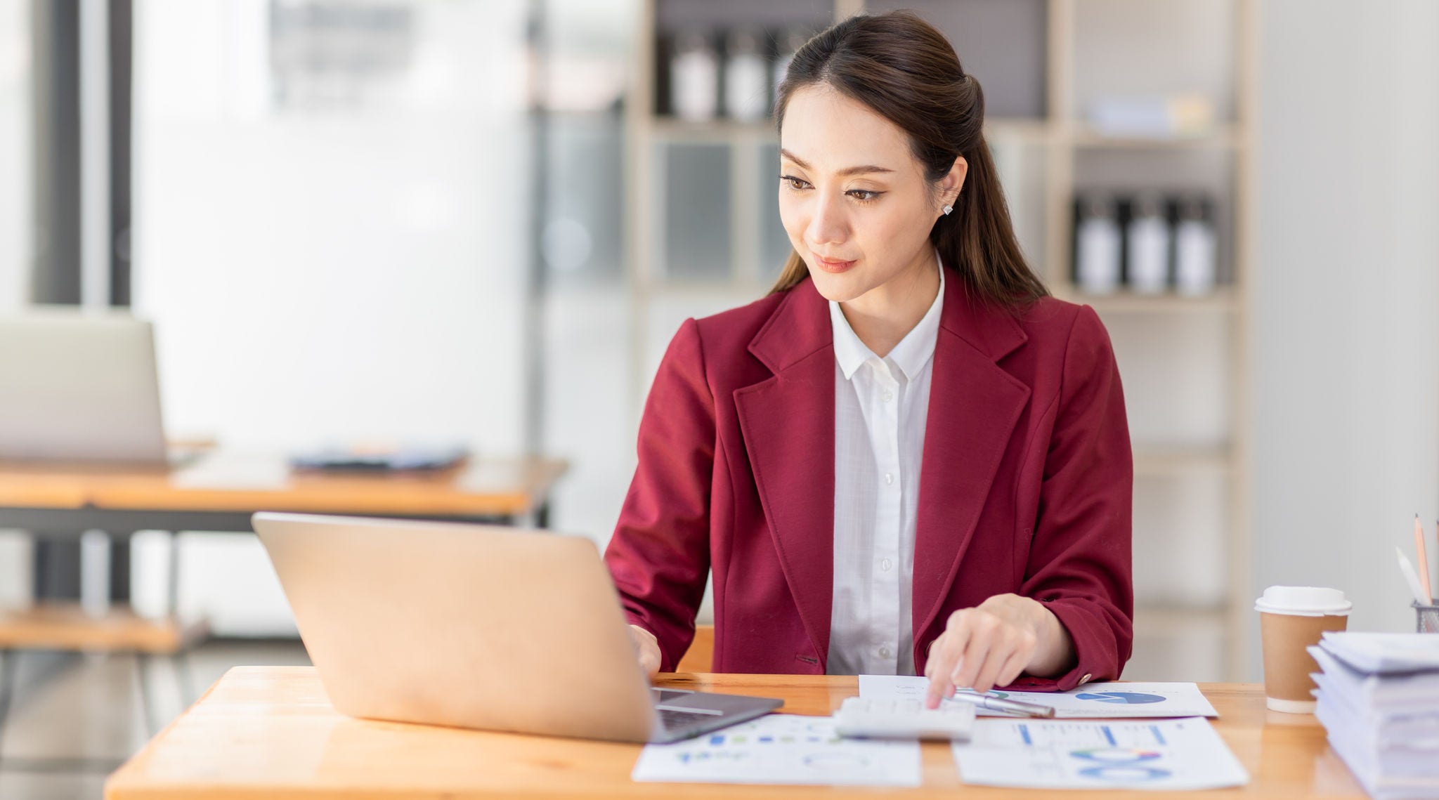 Asian woman working laptop in workplace, Business woman wearing red jacket suit busy working on laptop computer checking finances, investment, economy, saving money or insurance concept