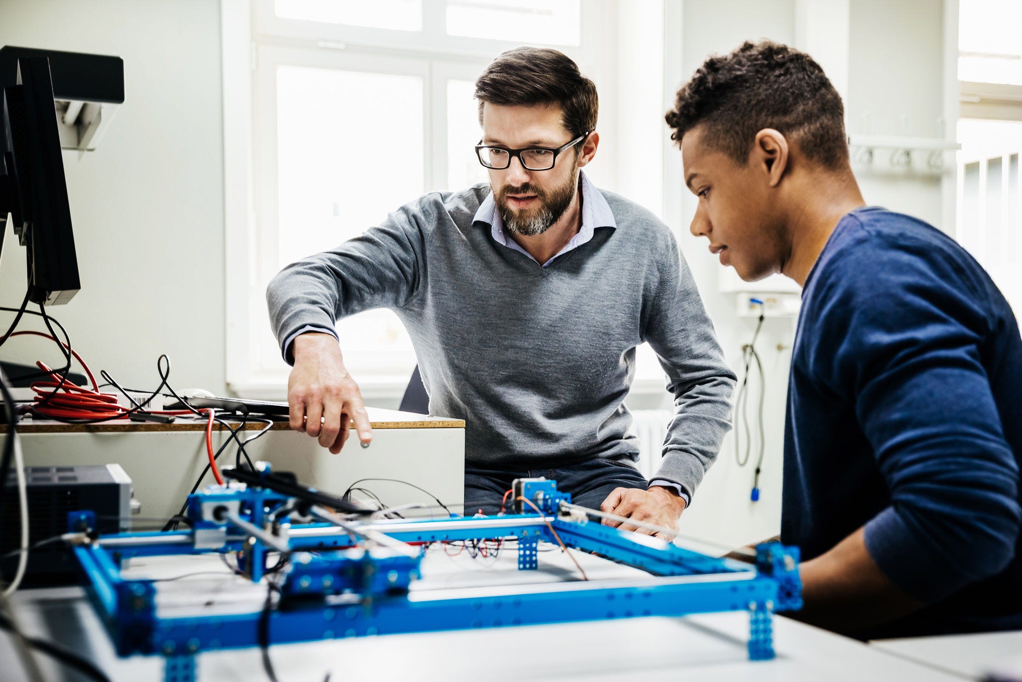 An engineering tutor assisting one of his students with a technical problem during teaching session at university.