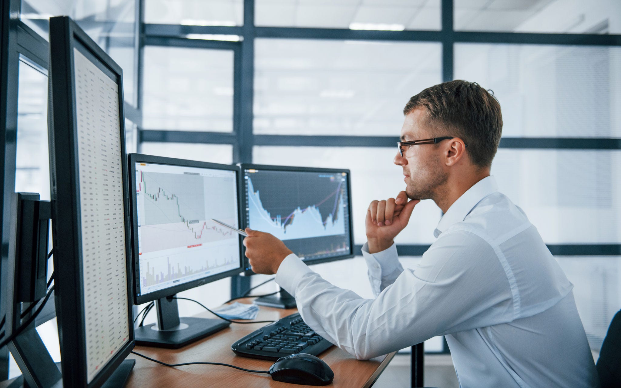 Analysing graphs. Young businessman in formal clothes is in office with multiple screens. Conception of exchange and money.