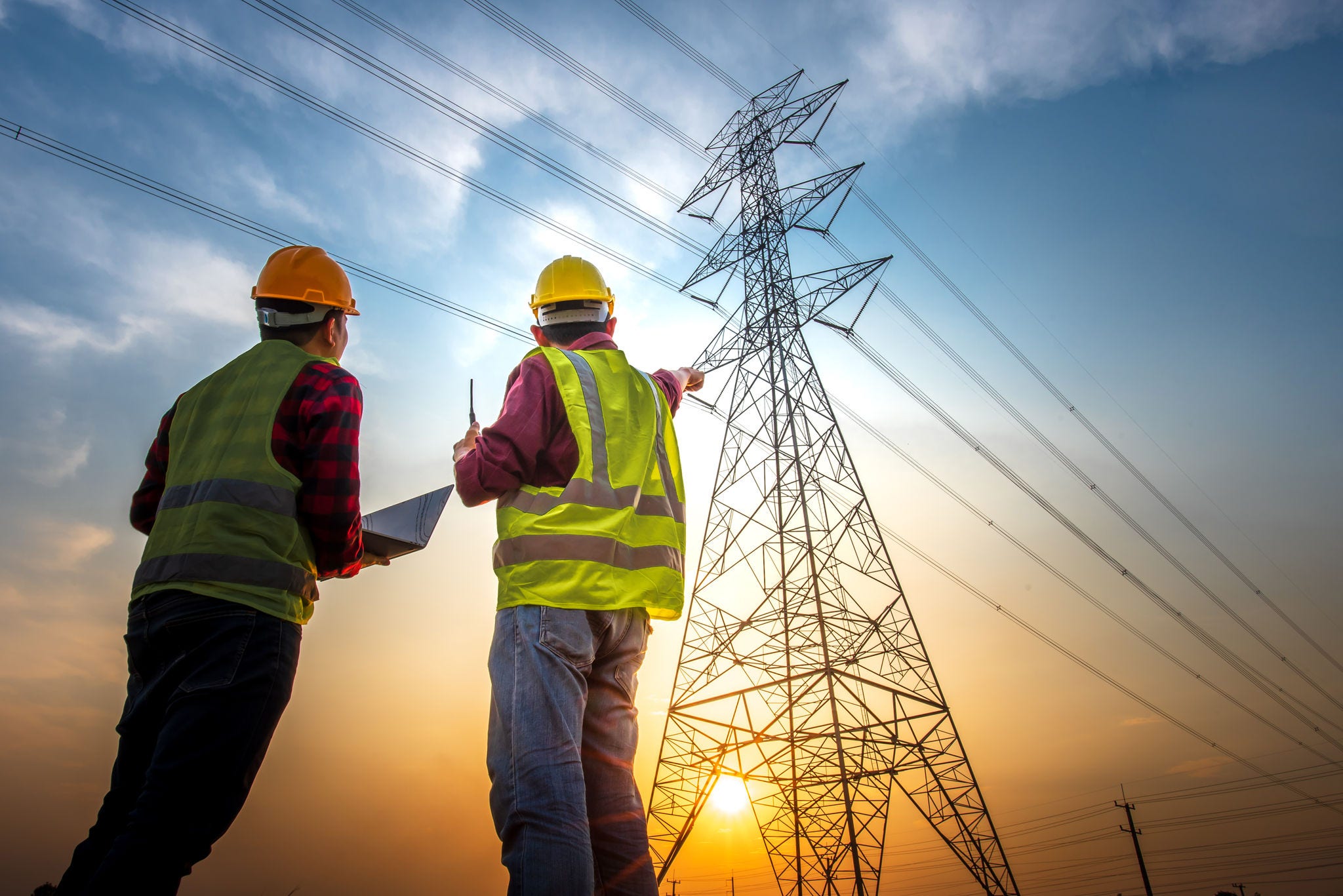 Picture of two electrical engineers using a notebook computer standing at a power station to view the planning work by producing electrical energy at high voltage electrodes.