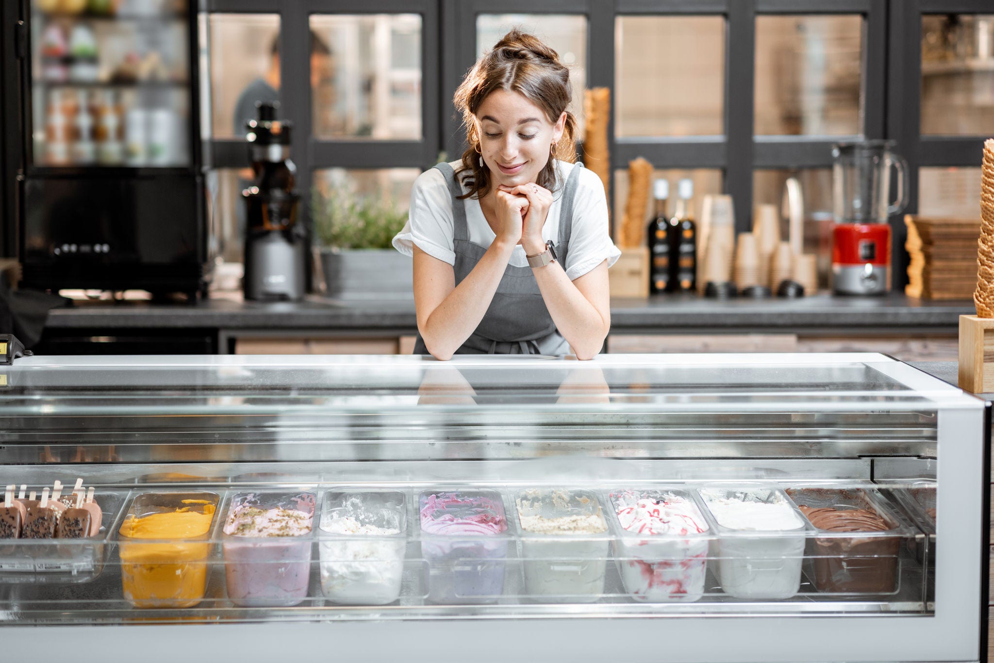 Portrait of a young and happy saleswoman at the counter in ice cream shop or cafe. Concept of a small business and retail