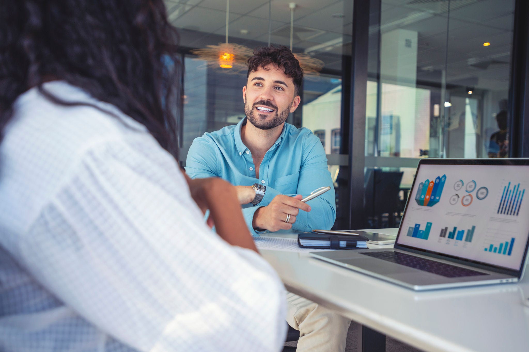 Business colleagues having a conversation. They are discussing a charts and graphs on a laptop computer. They are both young business people casually dressed in an office. Could be an interview or consultant working with a client.
