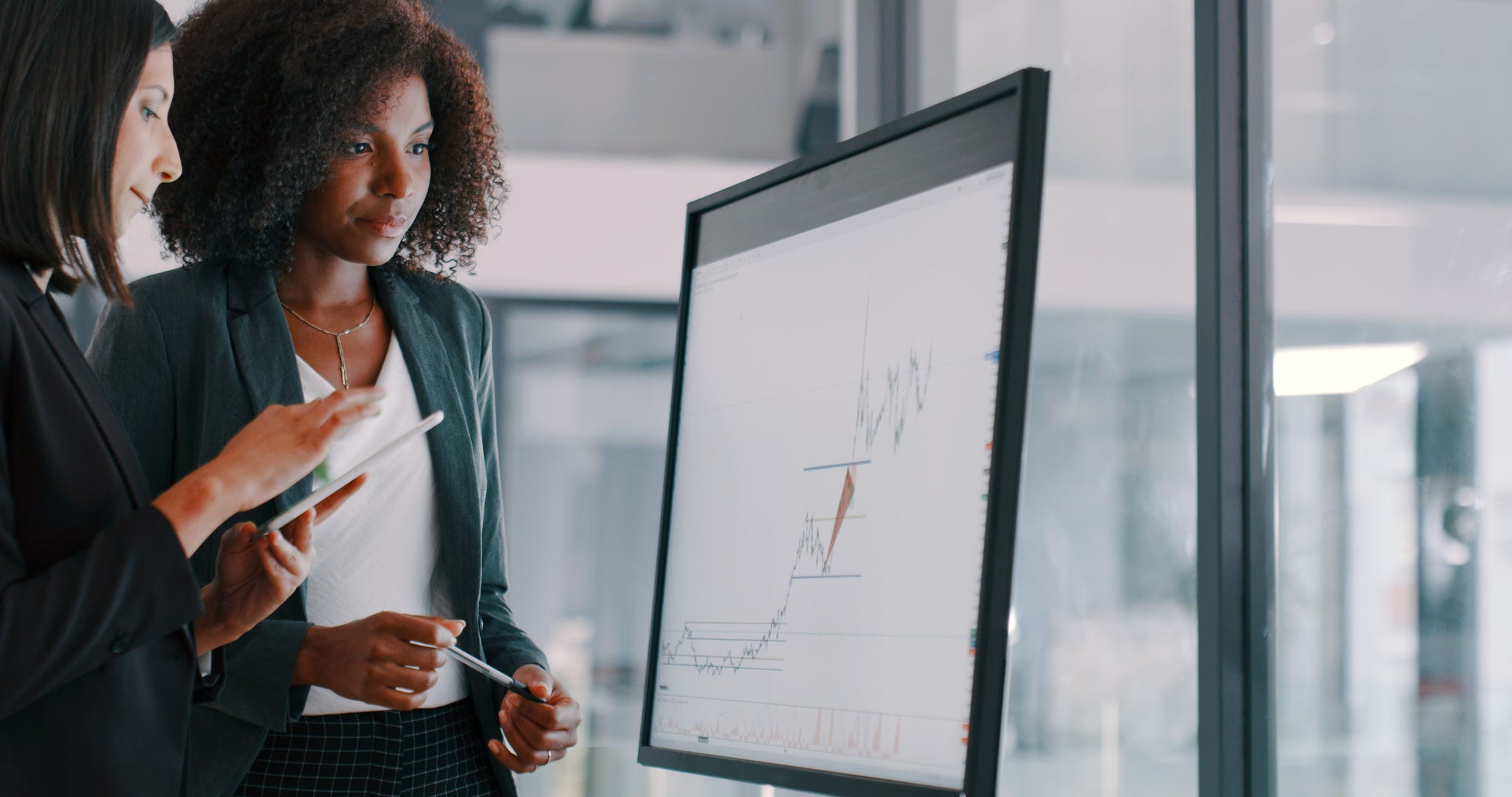 Shot of two young businesswomen using an interactive whiteboard to analyse data in a modern office